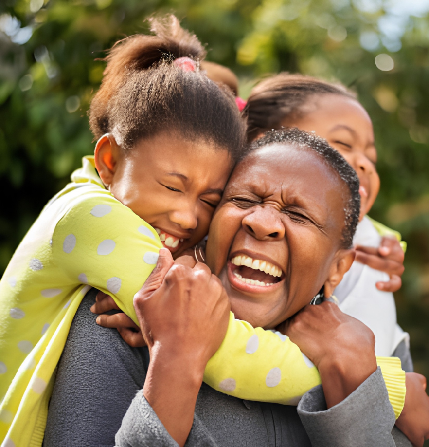 A grandmother laughing while being hugged by two grandchildren outdoors