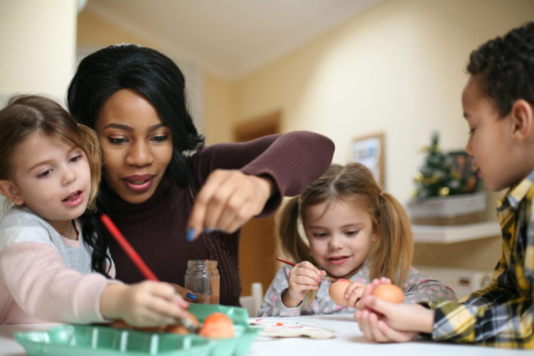 A nanny guiding children through an arts and crafts activity at a table