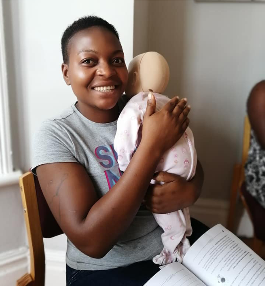 A smiling Super Nannies trainee practising infant care with a manikin