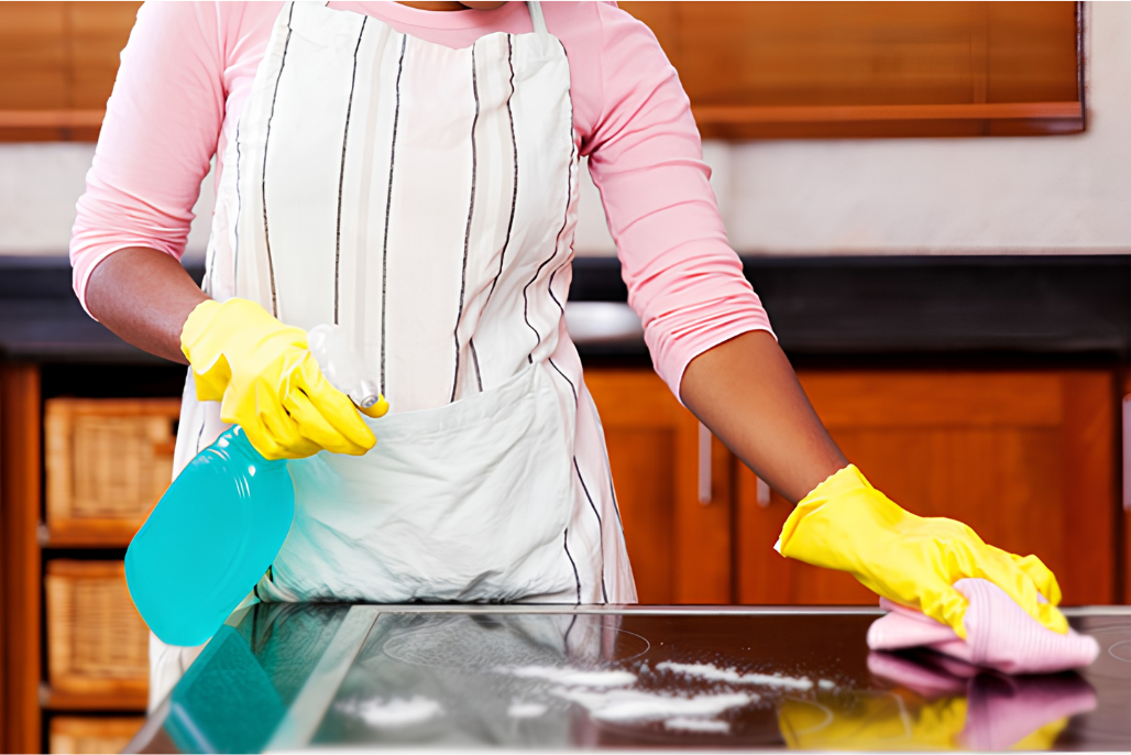 A housekeeper in apron and yellow gloves cleaning a kitchen stovetop